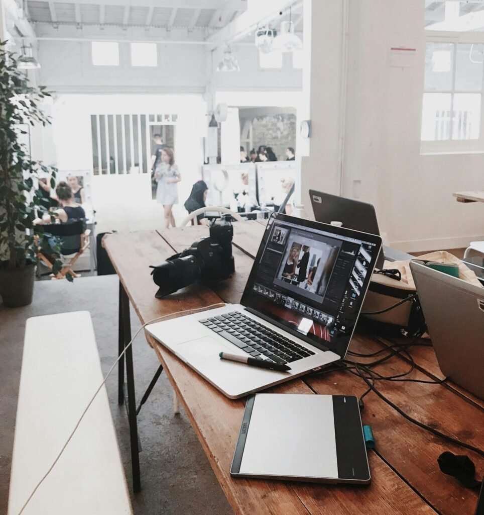 A bright, modern workspace featuring laptops, a camera, and a drawing tablet in an indoor office.
